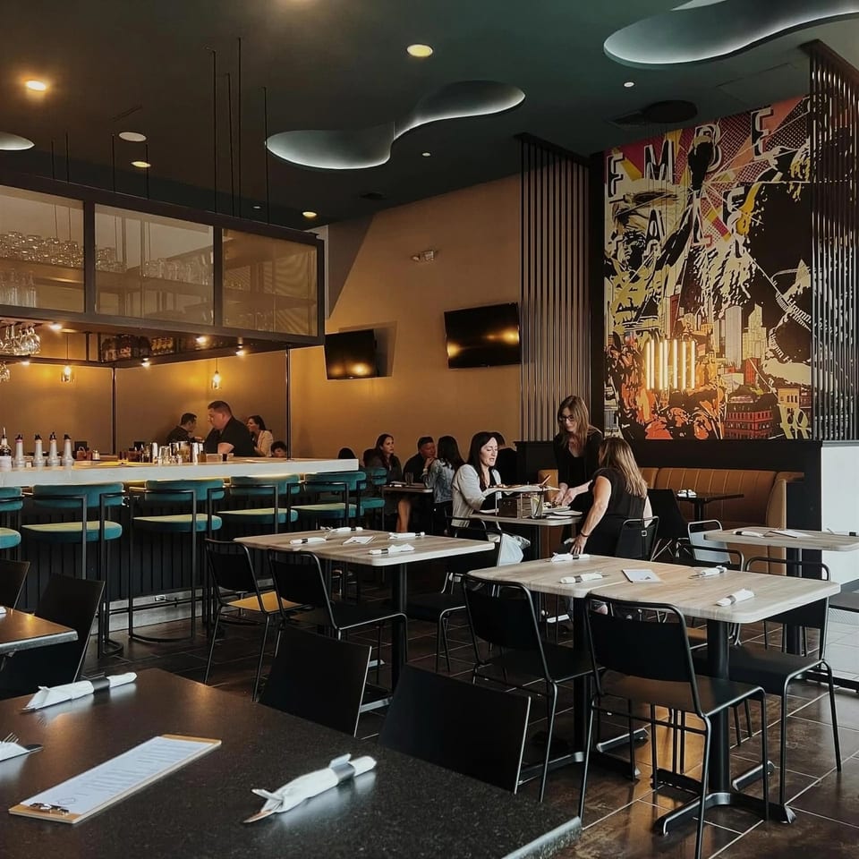A modern restaurant interior with a bar, dining tables, and a large colorful mural on the wall.