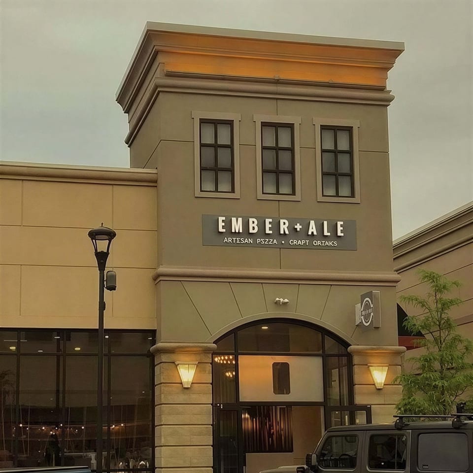 Exterior of Ember + Ale restaurant with a prominent sign, arched entrance, and large windows.