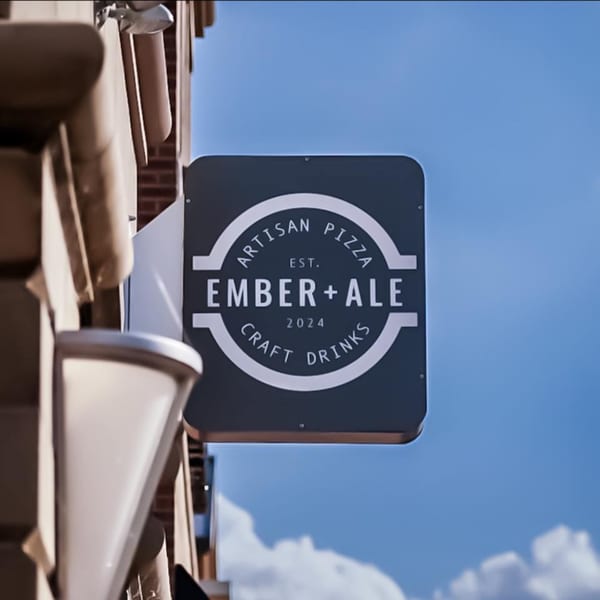Ember + Ale restaurant sign, a dark square with white text, against a blue sky.