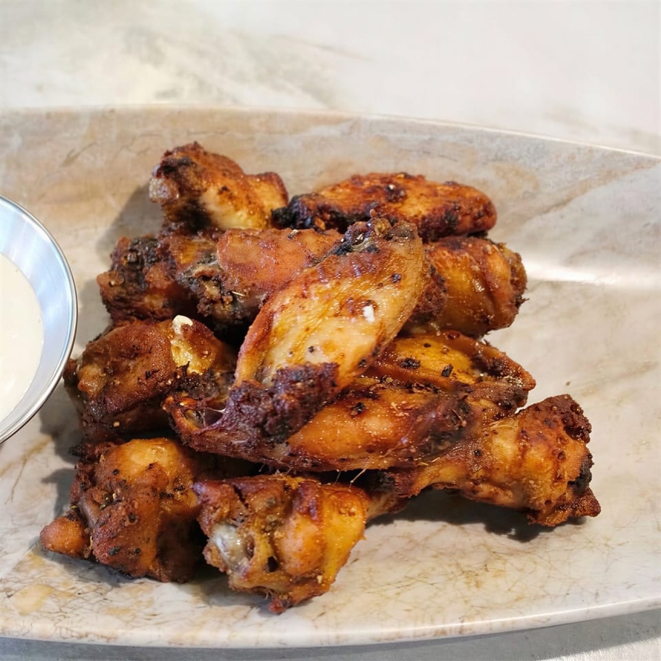A platter of crispy, seasoned chicken wings with a side of ranch dipping sauce.