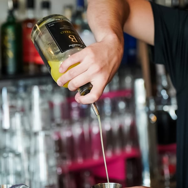 A bartender pours a yellow liquid from a bottle into a metal jigger at Ember + Ale.