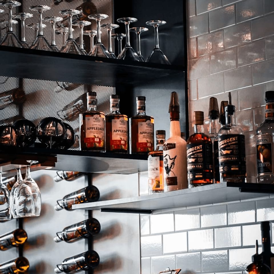 A bar shelf with various liquor bottles, including Applejack, and hanging wine glasses.