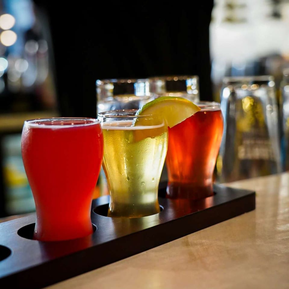 Three colorful beer tasters, one with a lime, on a wooden paddle at Ember + Ale.