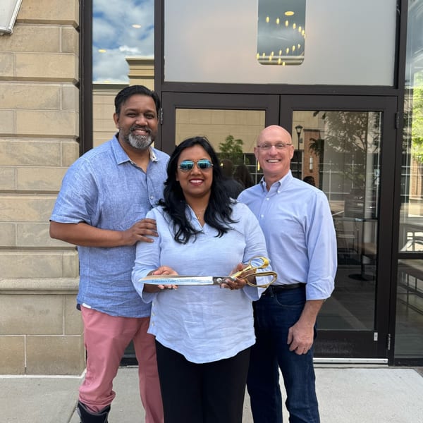 Three people, two men and one woman, stand outside Ember + Ale, holding large ceremonial scissors.