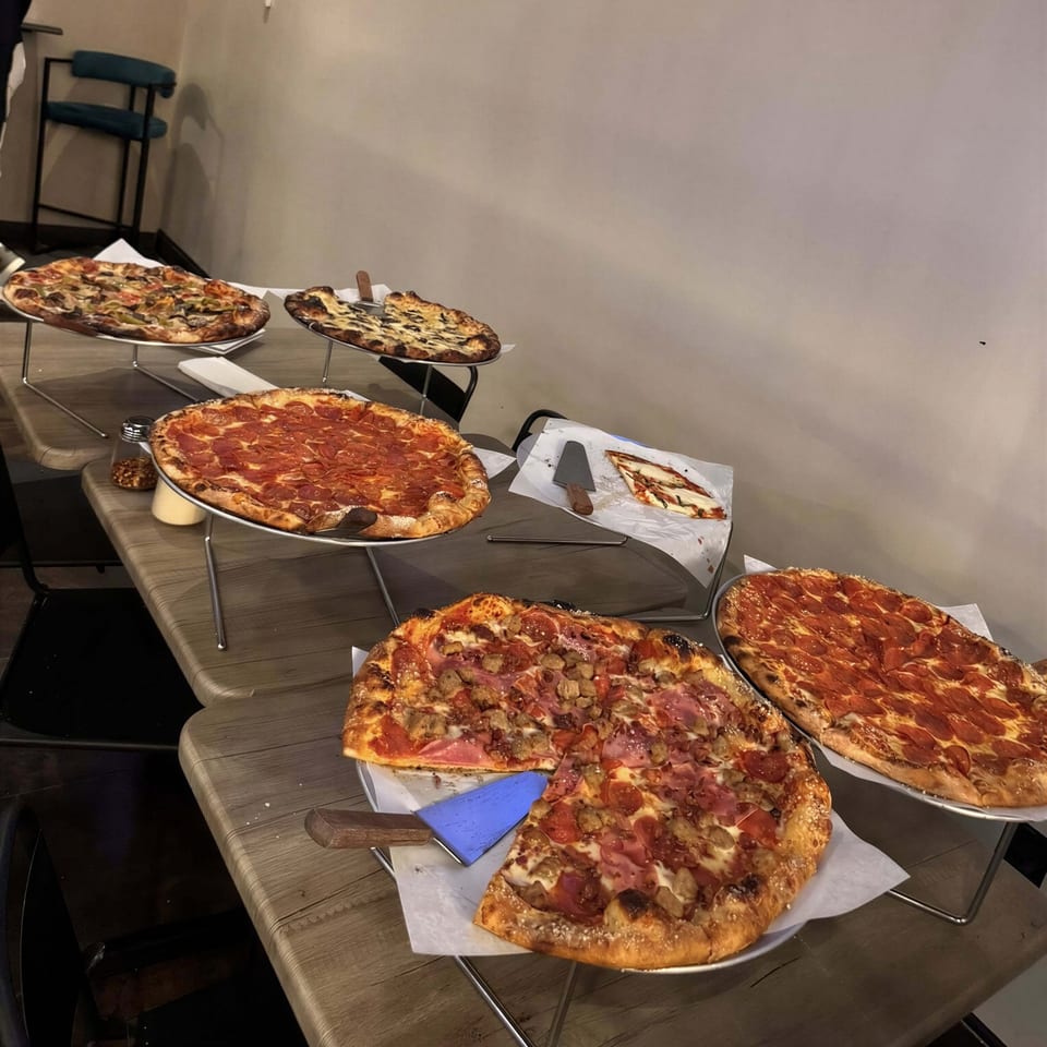 A variety of pizzas, including pepperoni, mushroom, and meat lovers, displayed on metal stands.