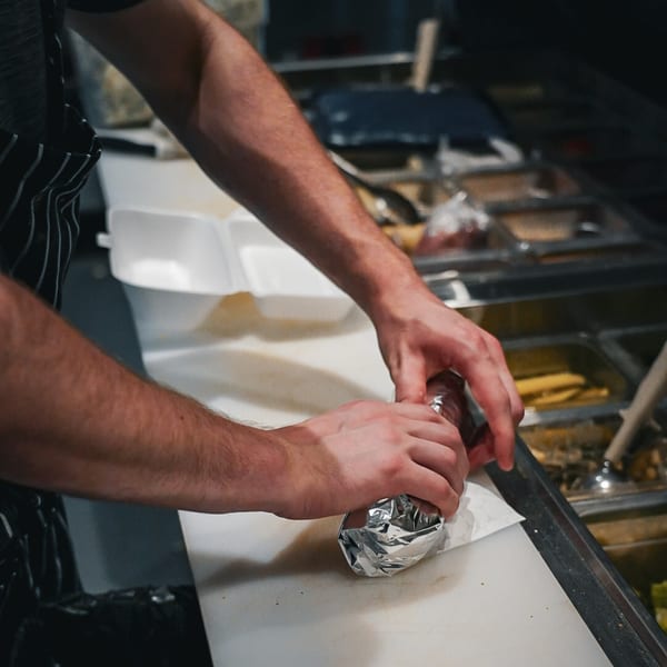 Chef's hands wrapping a pizza in foil and paper on a white cutting board.